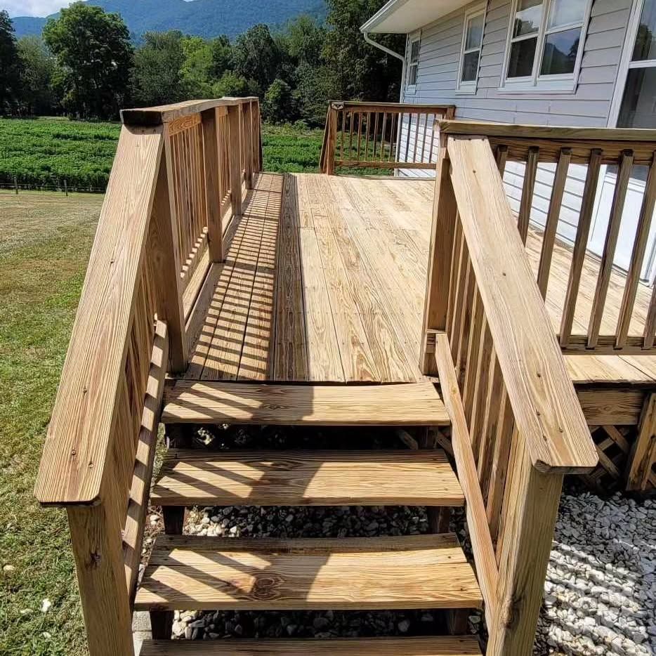 Wooden deck and stairs leading from a house, overlooking a field and mountains.