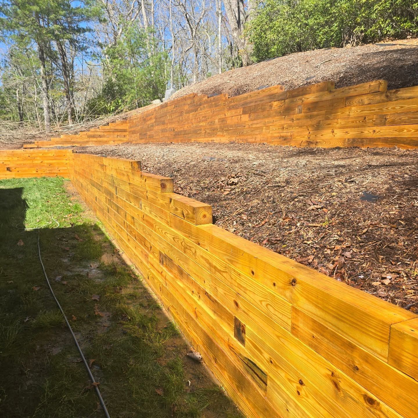 Wooden retaining wall with a grassy yard and hillside covered in mulch.
