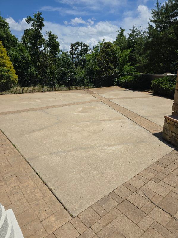 Concrete patio with brick border, surrounded by trees under a blue sky.