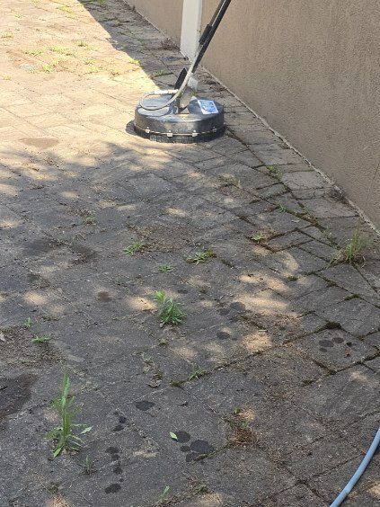 A person pressure washing a dirty brick patio next to a light brown wall.