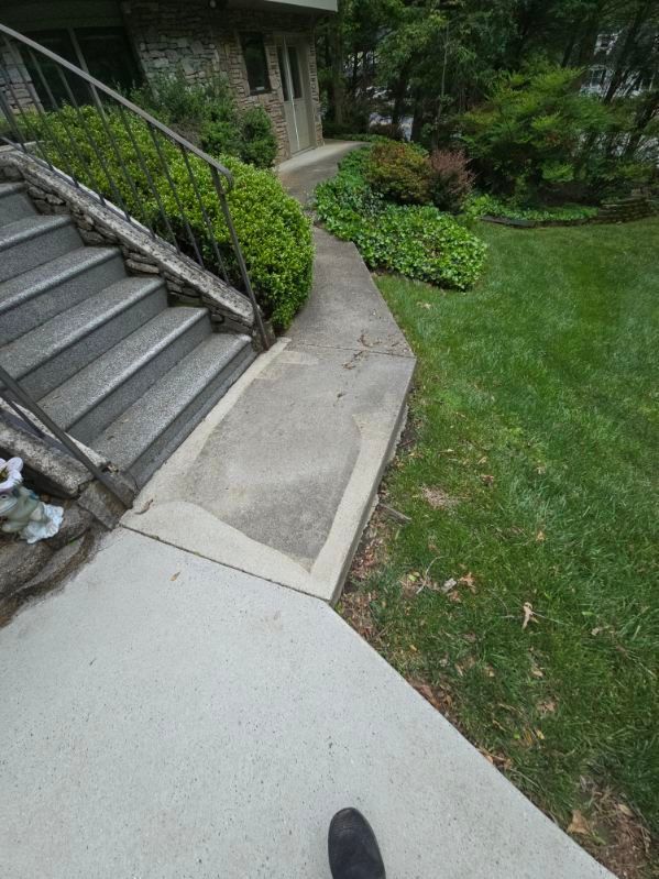 Concrete steps and walkway lead to a house with a green lawn and shrubs.