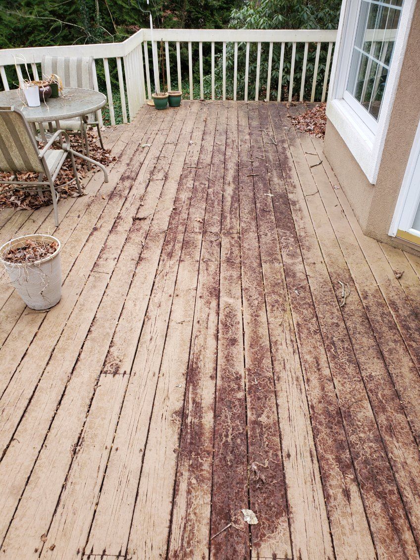 Wooden deck with leaves and potted plants; near house and railing. Brown wood with visible wear.