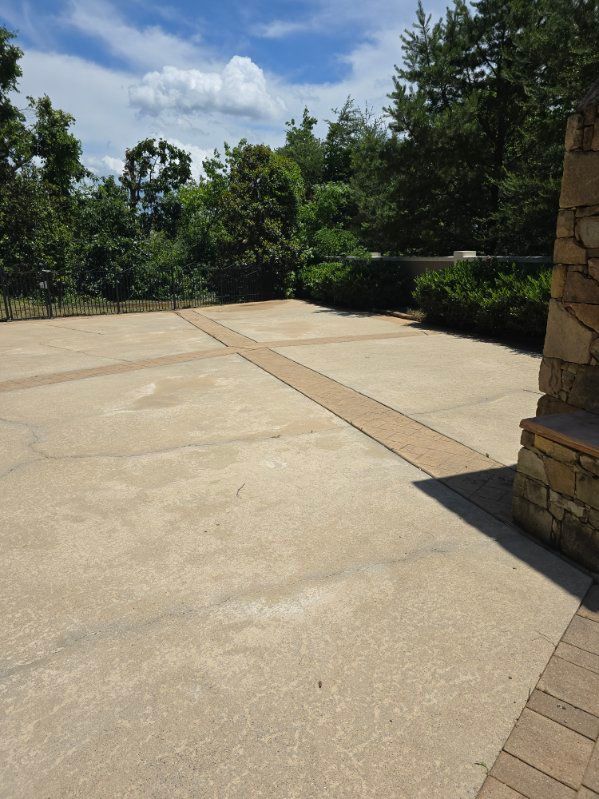 Large, light concrete patio with a stone accent. Trees and blue sky in the background.