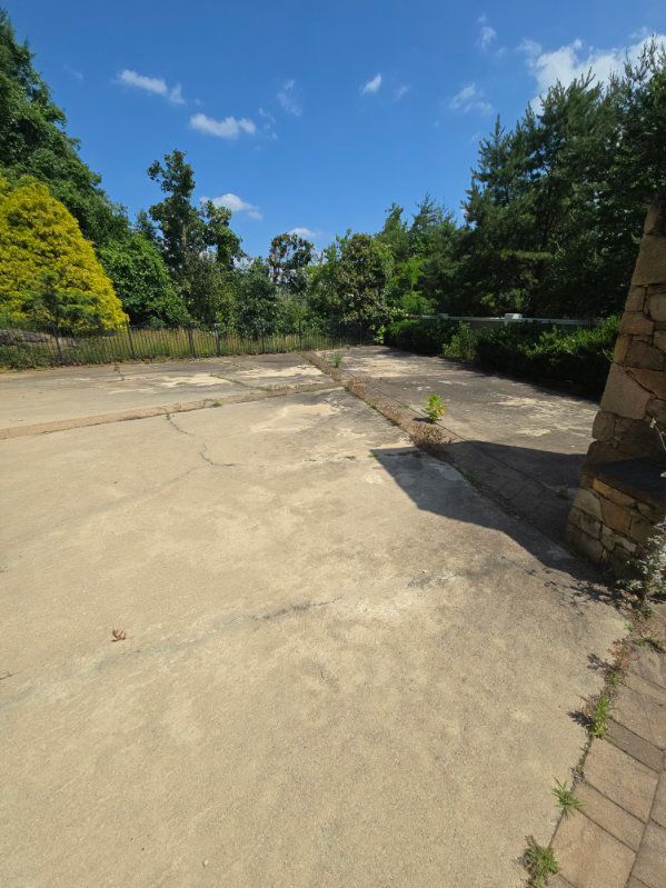 Concrete area surrounded by trees and bushes under a blue sky with scattered clouds.