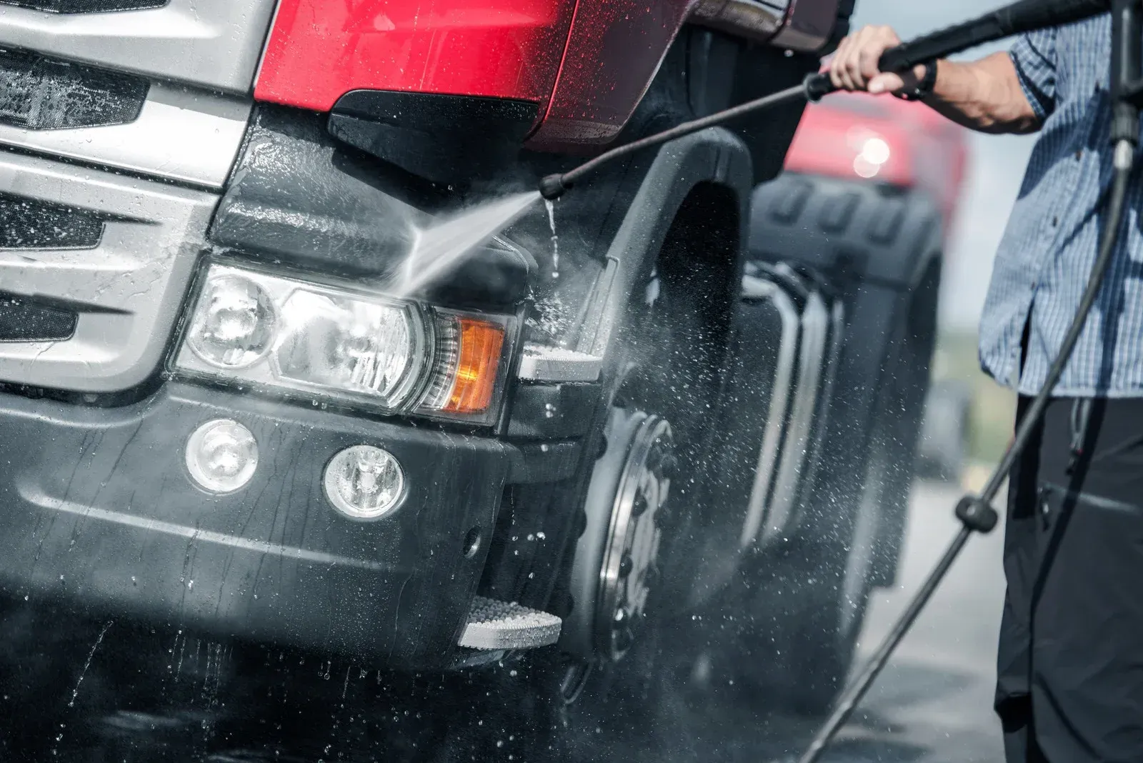 Person washing a red and black truck with a power washer. Water spraying on the front.
