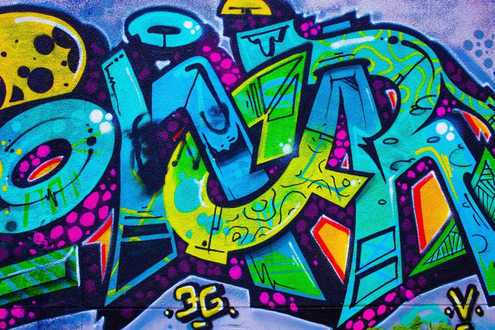 Colorful graffiti art with layered letters in teal, green, and purple on a wall.