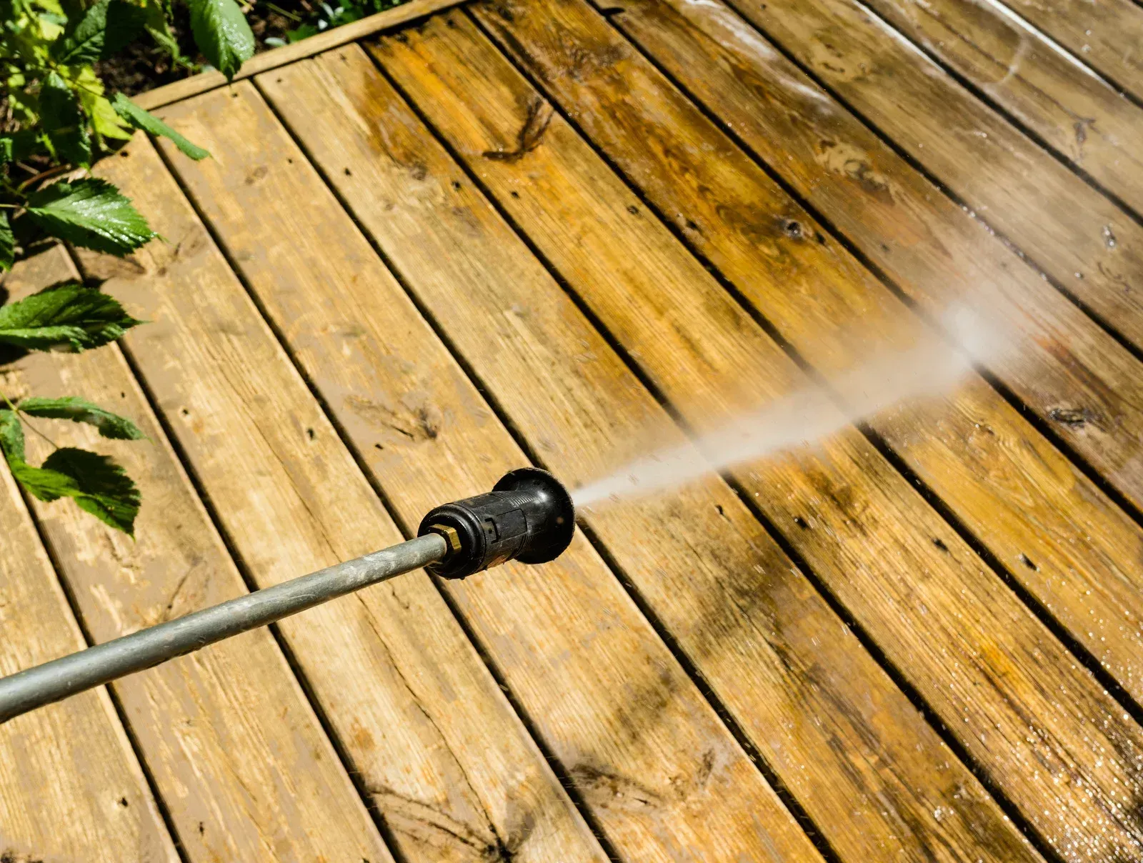 Pressure washing wooden deck with spray of water.