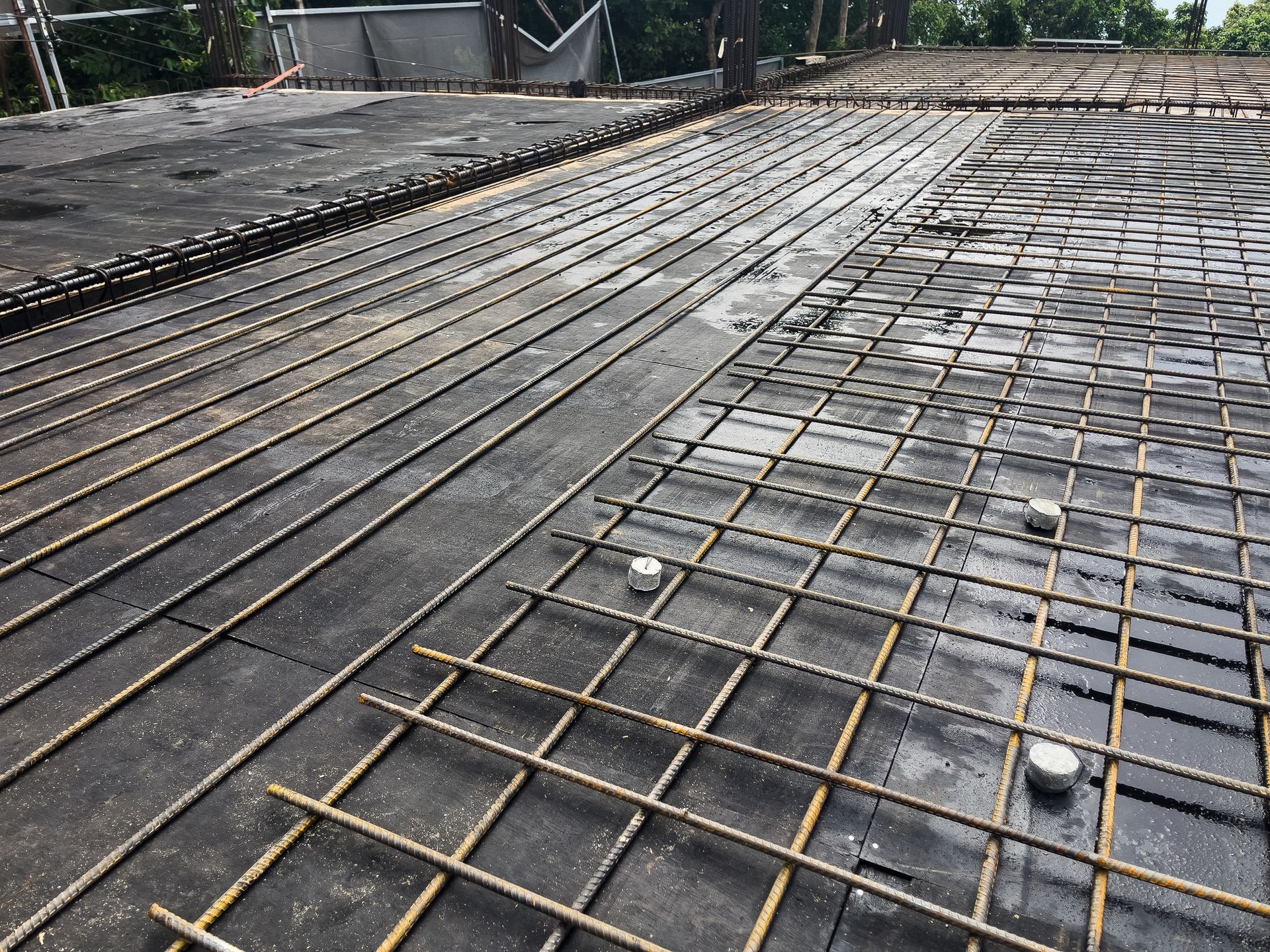 Steel rebar grids arranged over black formwork, prepared for pouring concrete slabs
