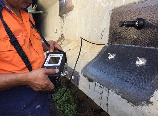 A man in an orange shirt is holding a device in front of a sink