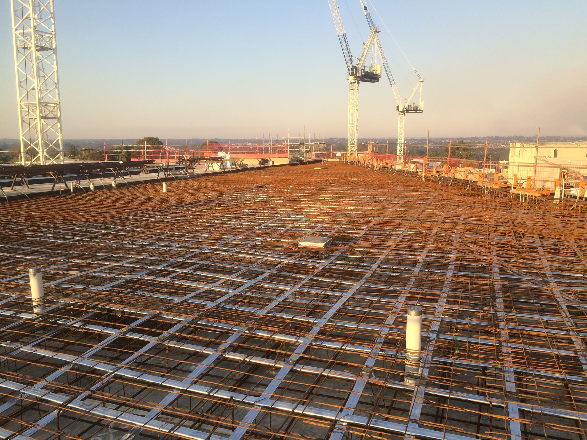 The roof of a building under construction with cranes in the background.