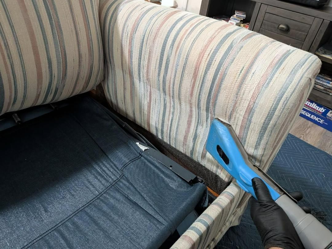 Person cleaning a striped upholstered couch with a blue cleaning tool.