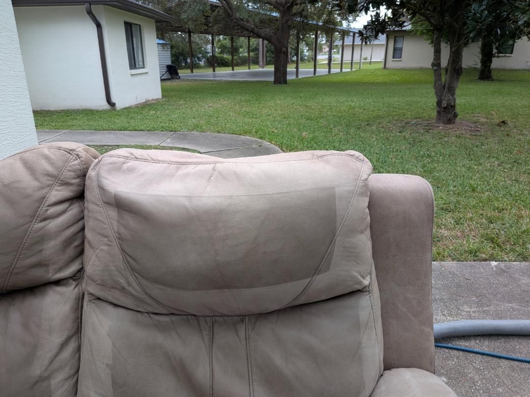 Tan upholstered recliner chair outdoors on a concrete slab, with grass and houses in the background.
