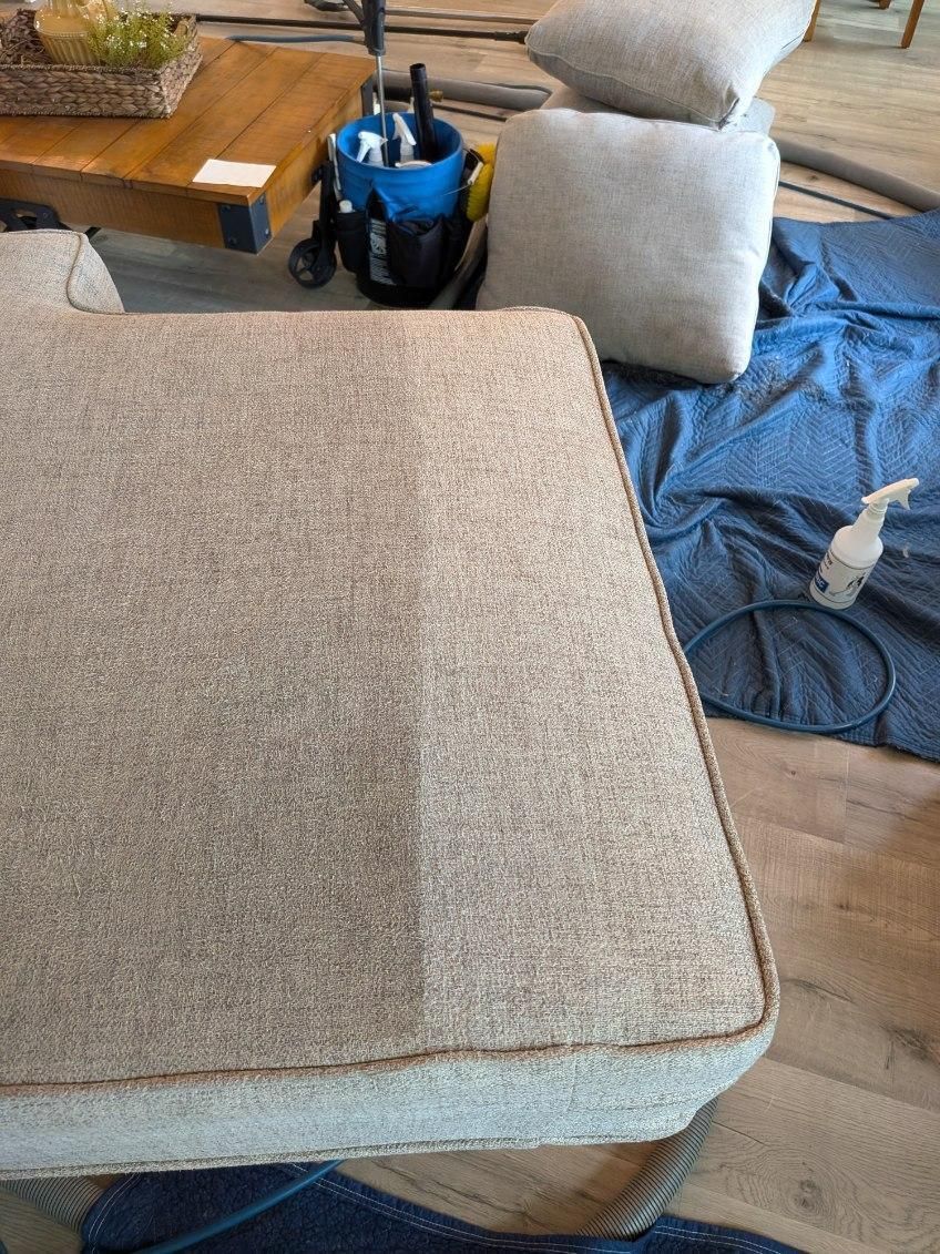 Sofa cushion, half cleaned, revealing a lighter color; cleaning supplies visible nearby.