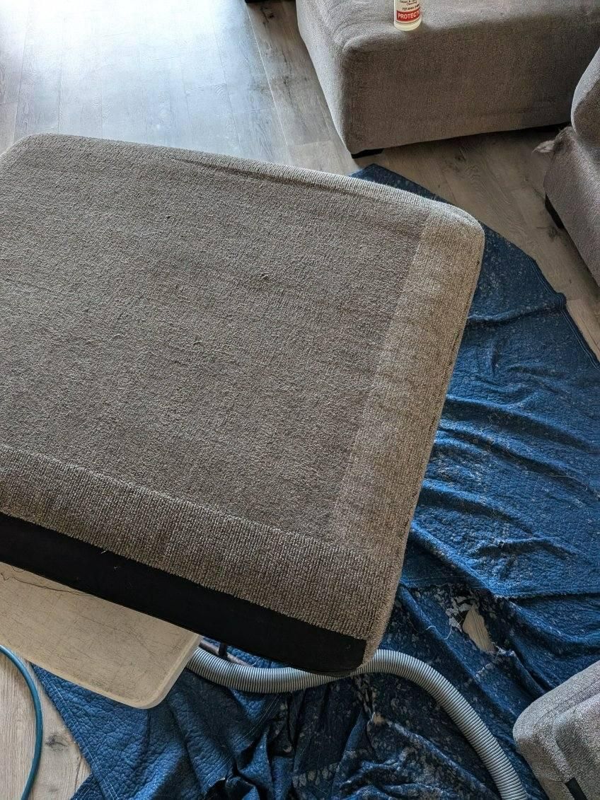 A carpeted furniture piece being cleaned with a machine; a blue sheet underneath.