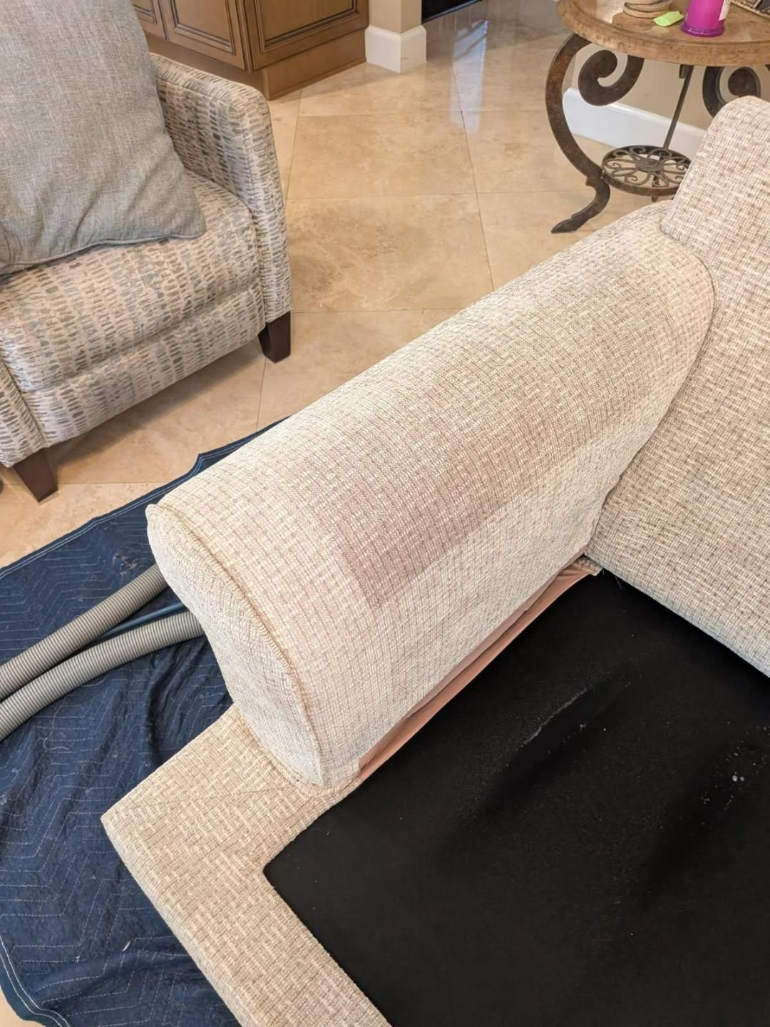 Beige sofa arm partially disassembled, revealing black cushion and exposed frame.