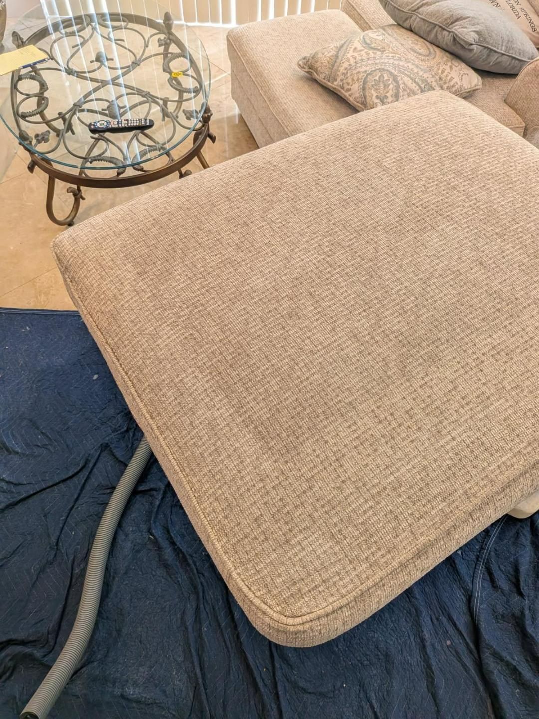 Beige couch cushion being vacuumed, sitting on dark blue fabric.