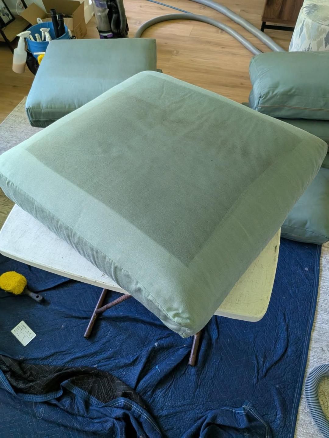 Cushion covered in green fabric on a small table, other cushions and tools in background.