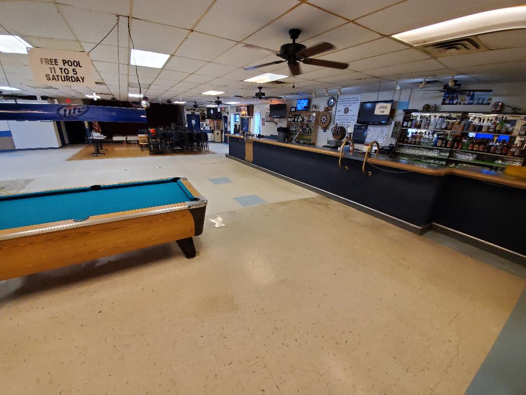 A bar with a pool table in the foreground; dark blue bar, cream floor and ceiling, multiple TVs.