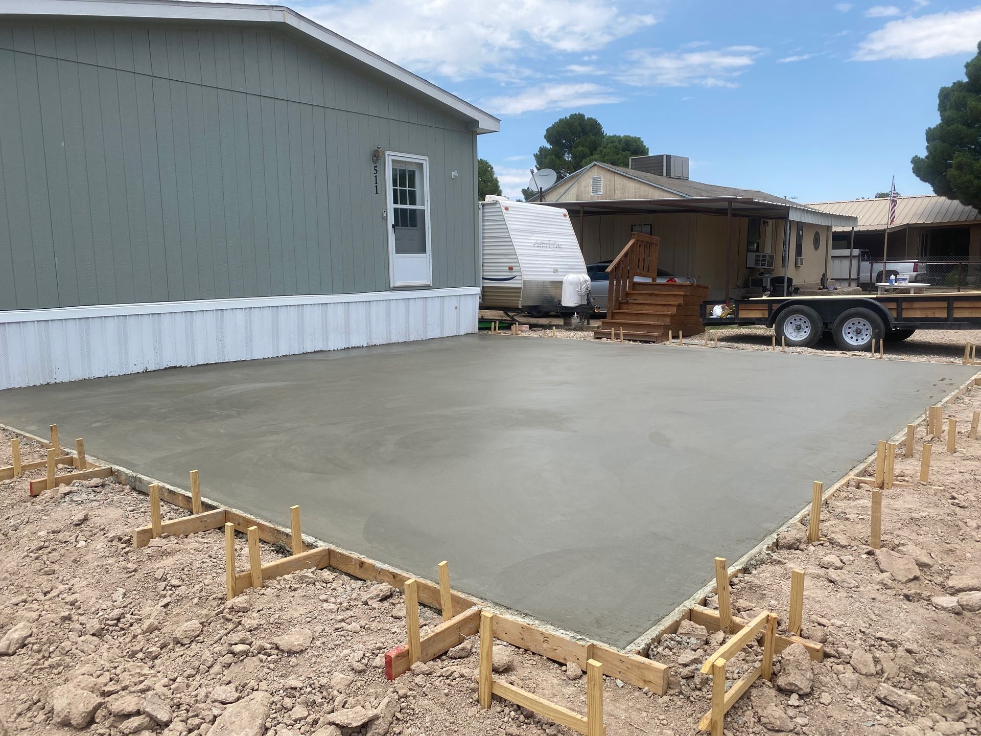 Newly poured concrete patio next to a light green mobile home. Forms are in place around the perimeter.