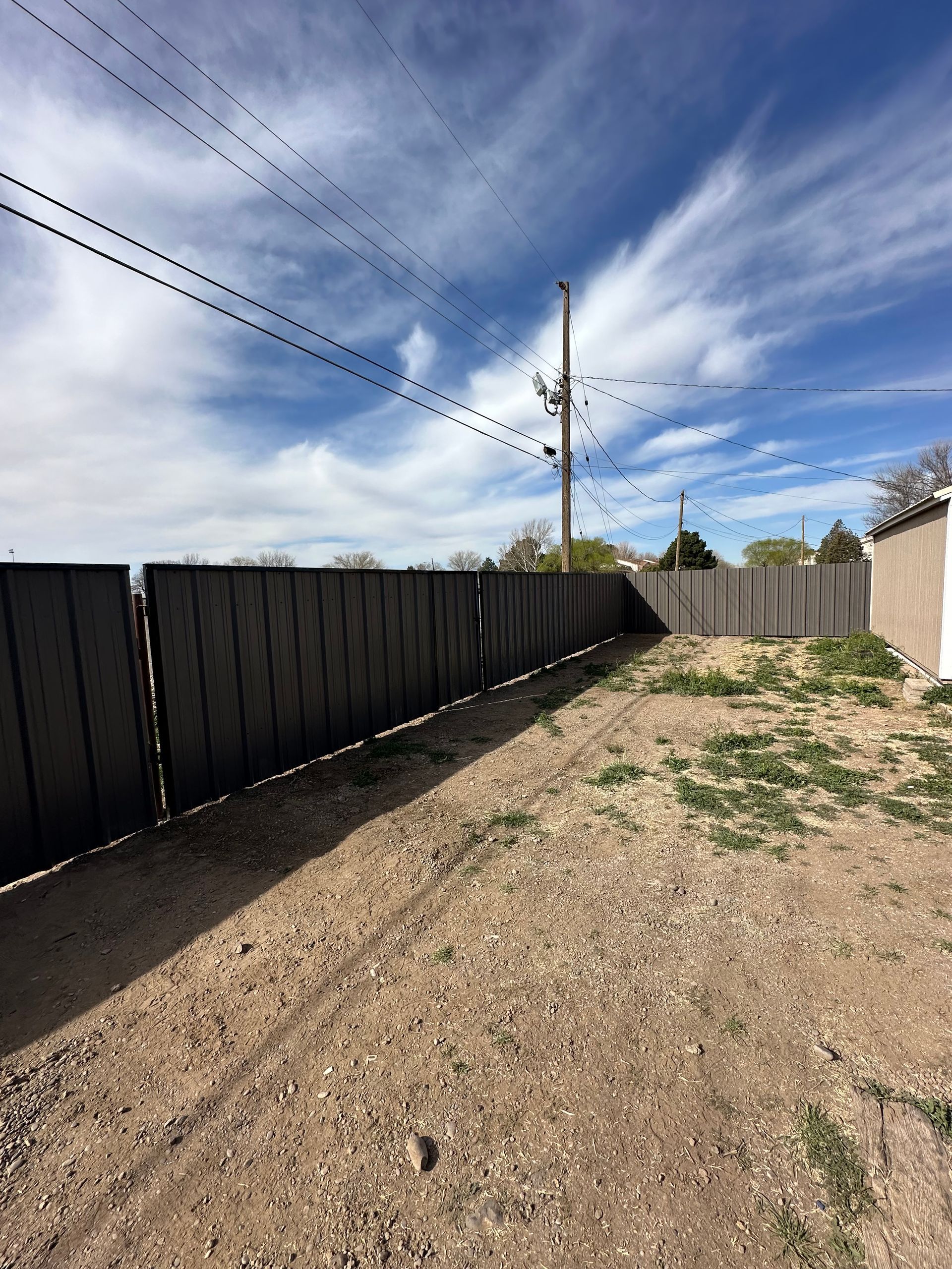 Gray wooden fence and dirt yard against a partly cloudy blue sky.