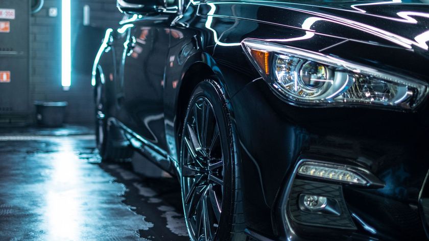Black car in a car wash with blue lighting, highlighting the front tire and headlight.