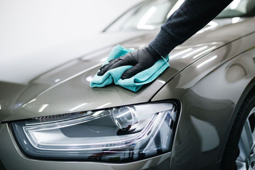 Person wearing black gloves wiping a gray car with a blue microfiber cloth.