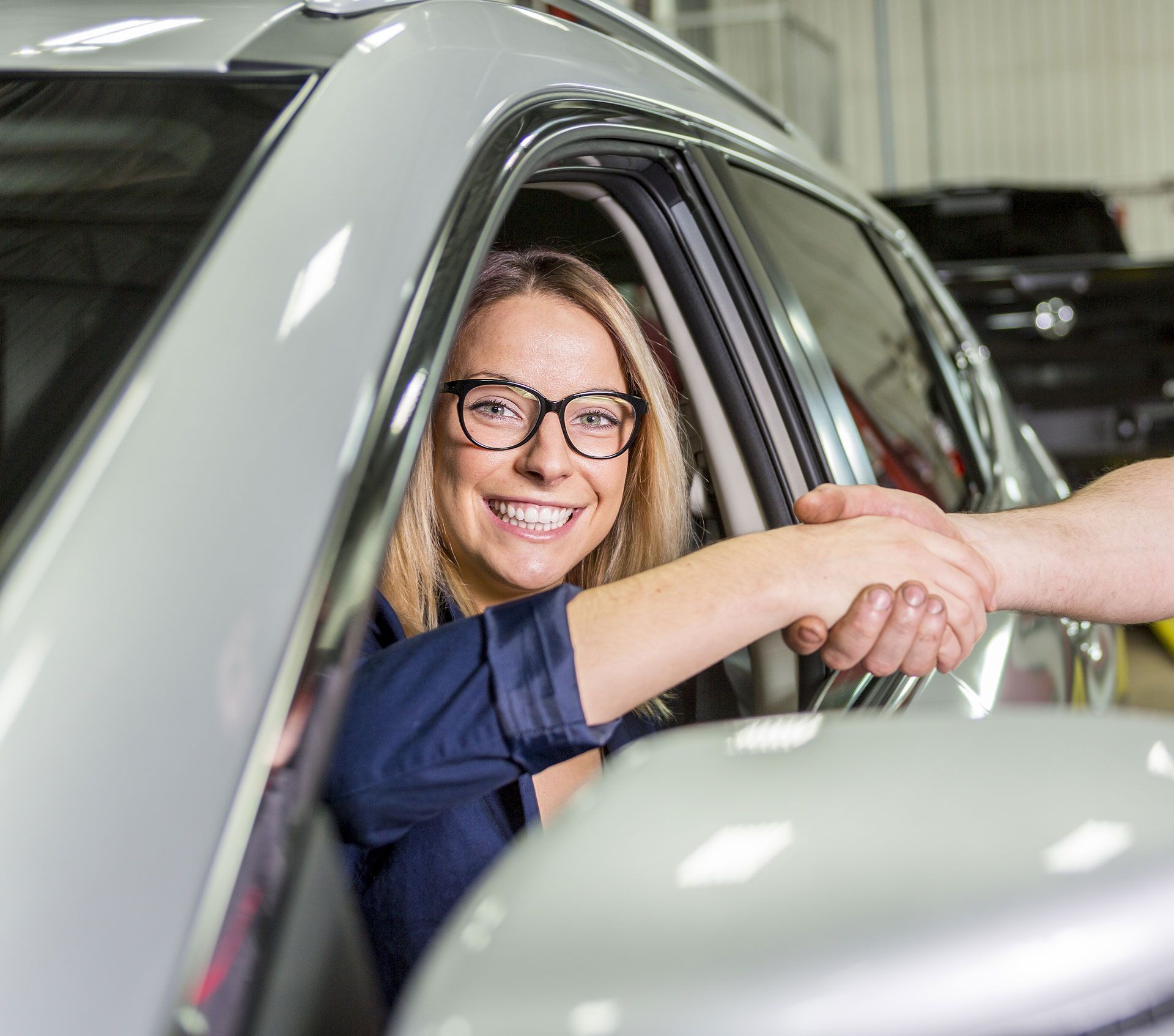 Woman in car shaking hands with someone, smiling.