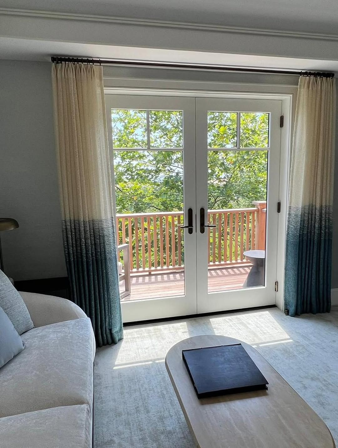 Interior with French doors to a balcony, adorned with cream and teal ombre curtains.