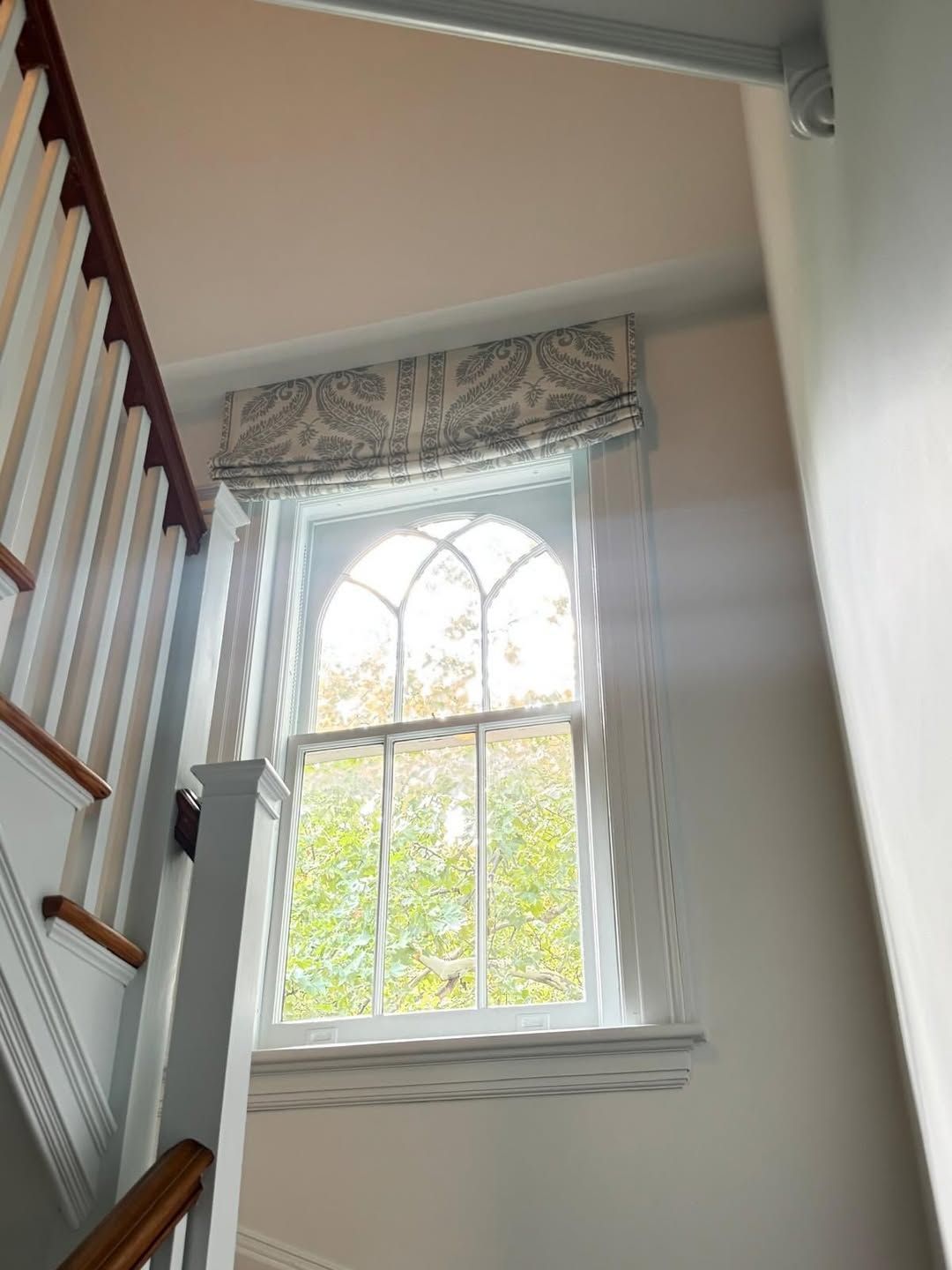 Window with white trim and paisley valance above staircase.