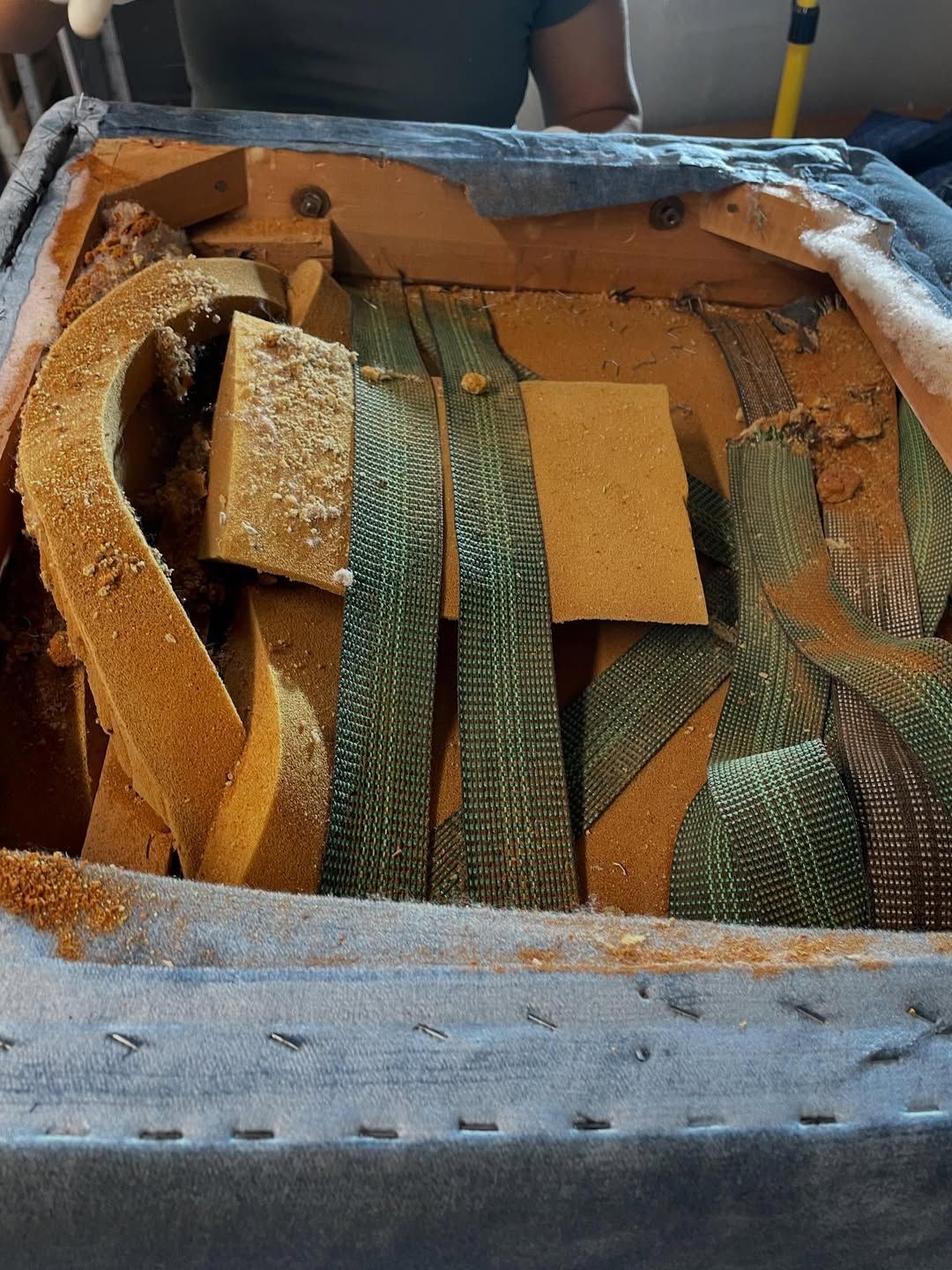 Open seat of a blue upholstered chair showing internal support structure of straps and foam.