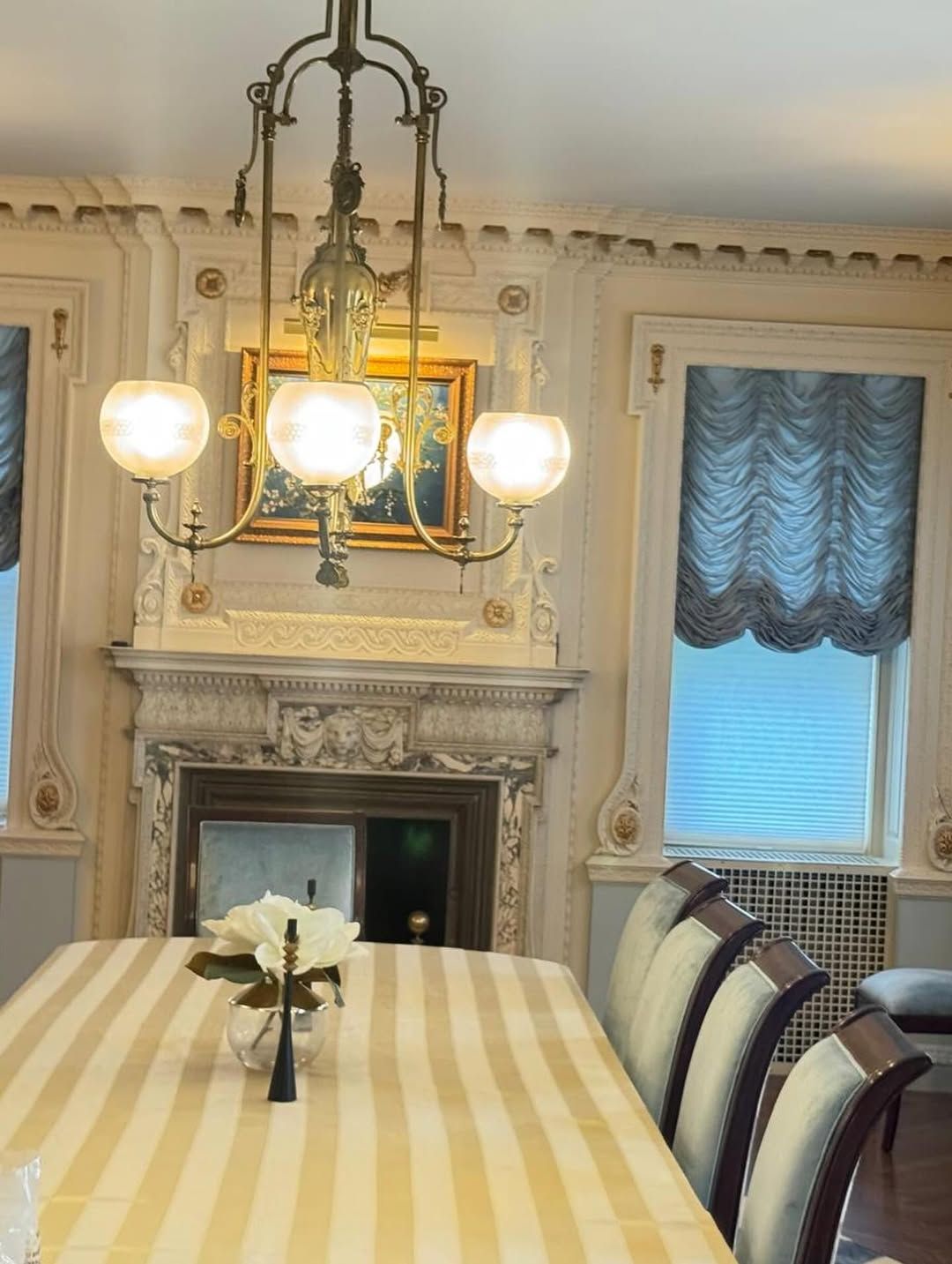 Elegant dining room with chandelier, fireplace, ornate trim, striped tablecloth, and window.
