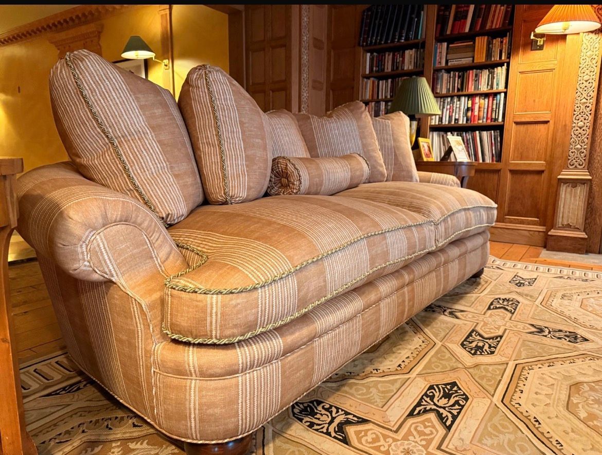 Tan striped couch in room with a bookshelf and ornate rug.