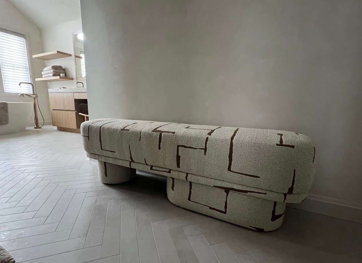 Upholstered bench with a patterned design, in a room with light-colored walls and flooring.