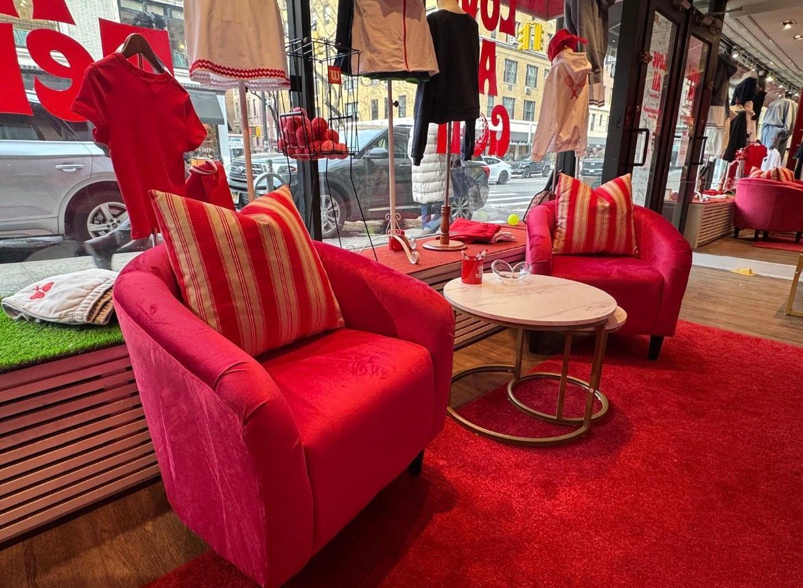 Two pink armchairs, red rug, small round table with a glass, clothes on display in a store window.