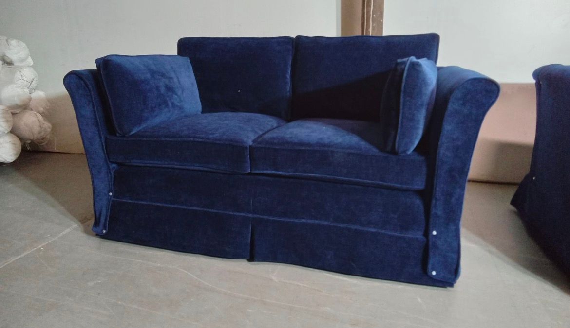 Navy blue velvet two-seater sofa with flared arms and skirted base. Pillow cushions are visible.