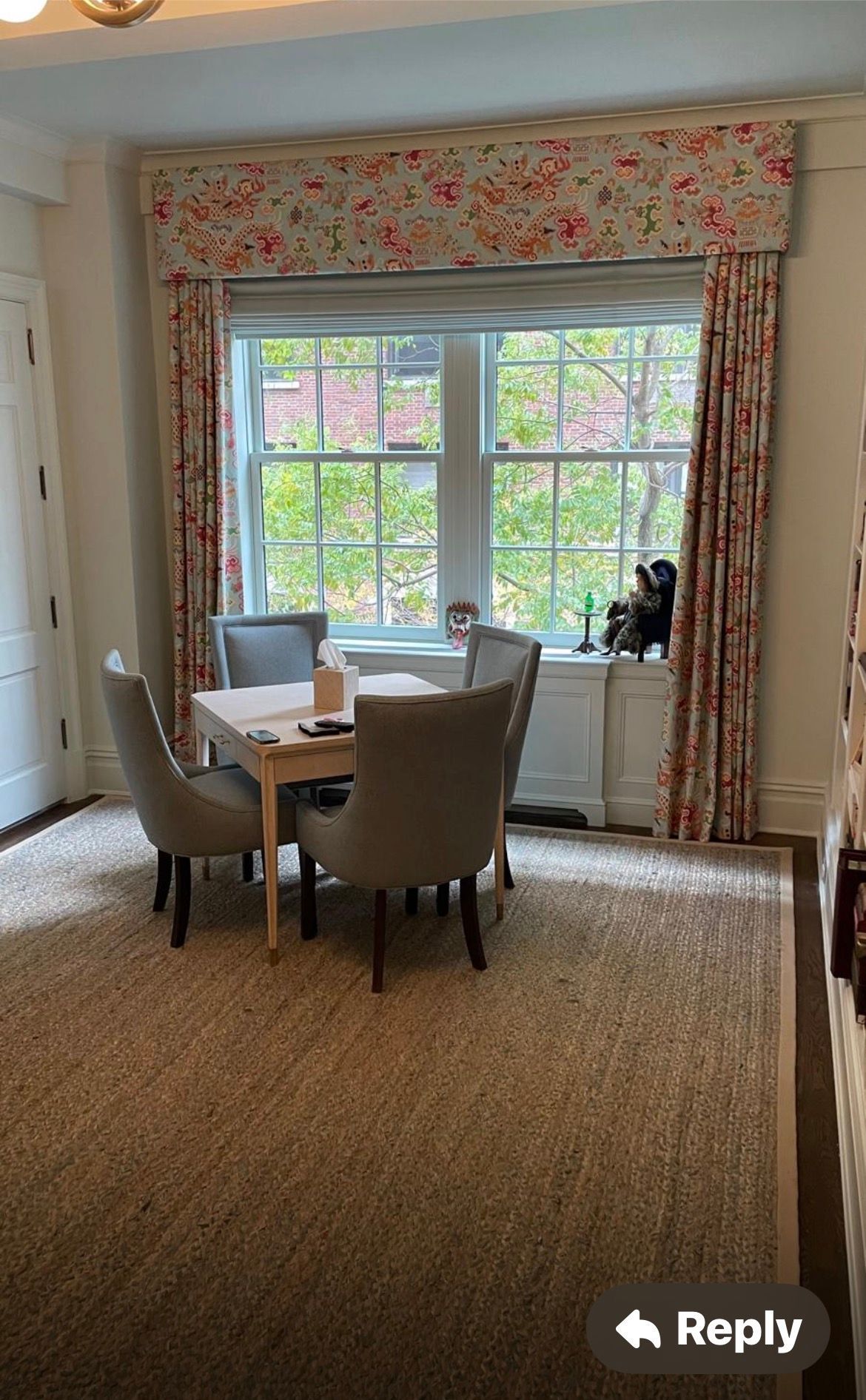 Dining room with a square table and four gray chairs, set in front of a window with floral patterned curtains and a shade.