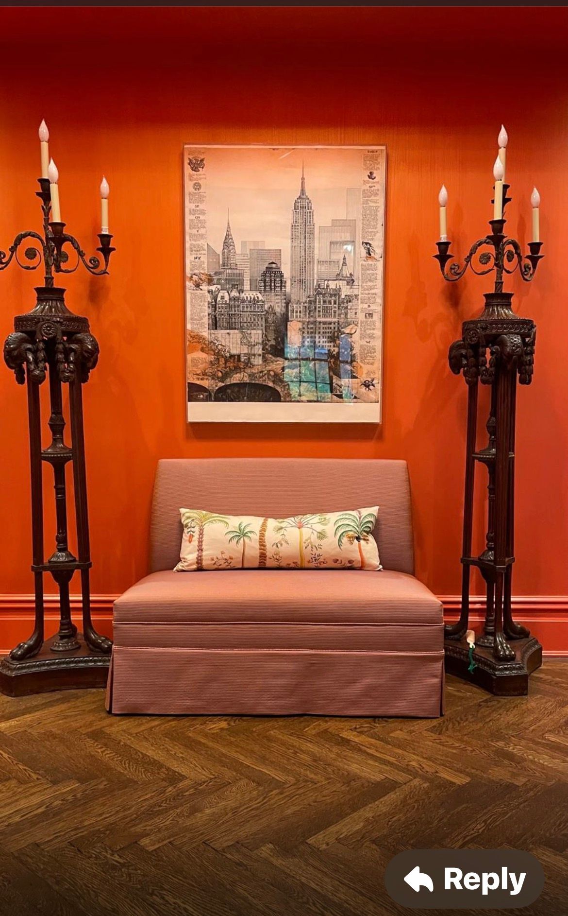 Orange wall with art, bench, and tall ornate candleholders flanking it.