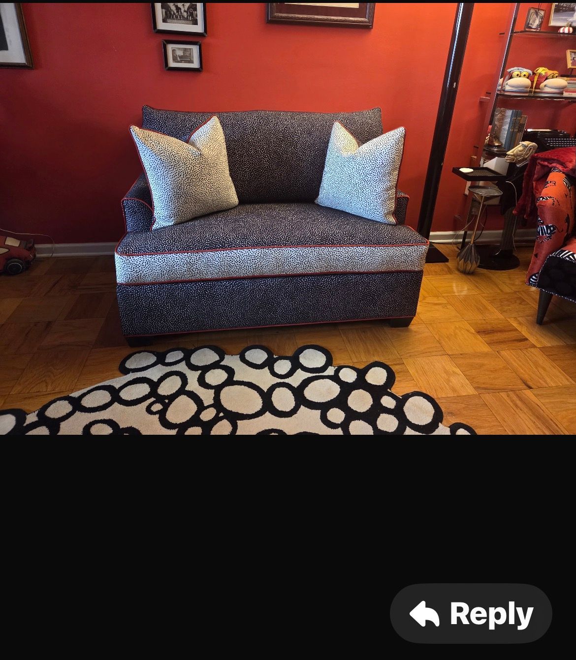Cozy living room with patterned armchair, pillows, and decorative rug on a hardwood floor, with red walls and artwork.