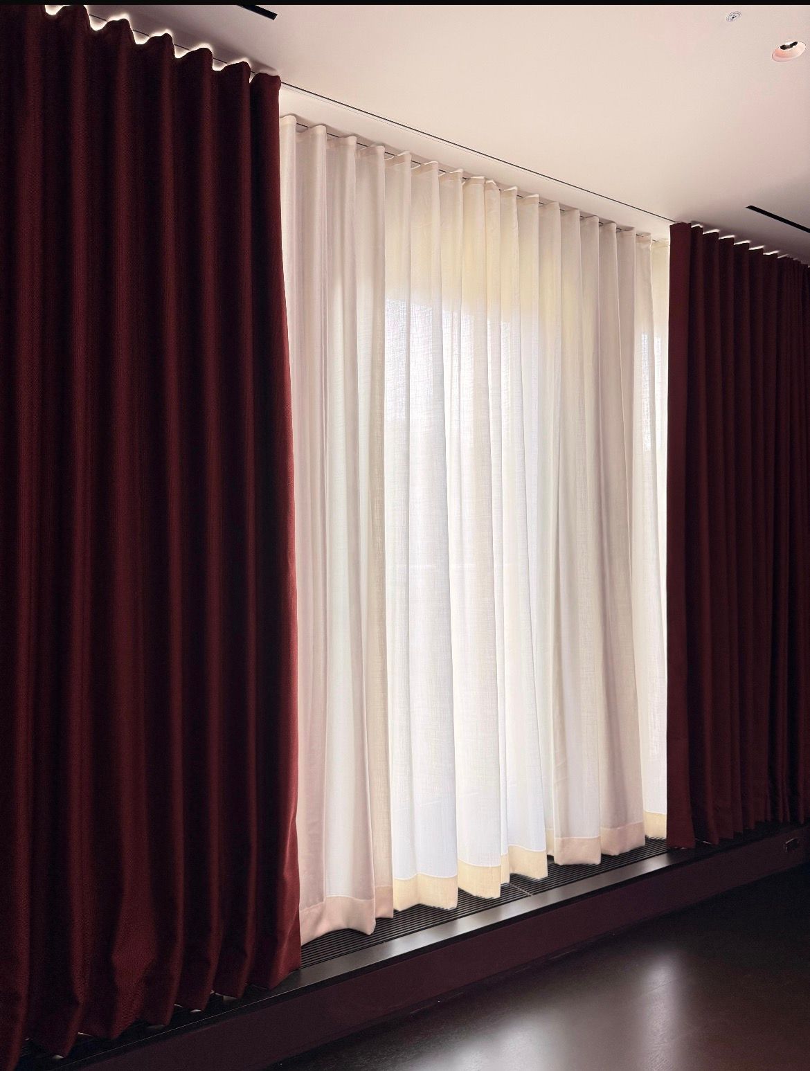 Burgundy curtains frame a sheer white curtained window. A dark room is in view.