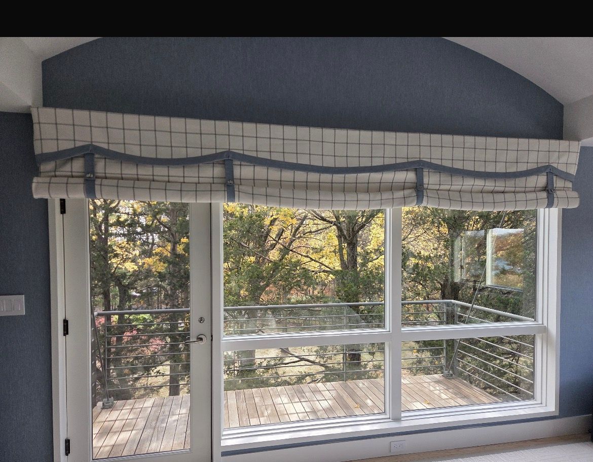 Window with grid-patterned Roman shade and view of trees, deck, and railing.