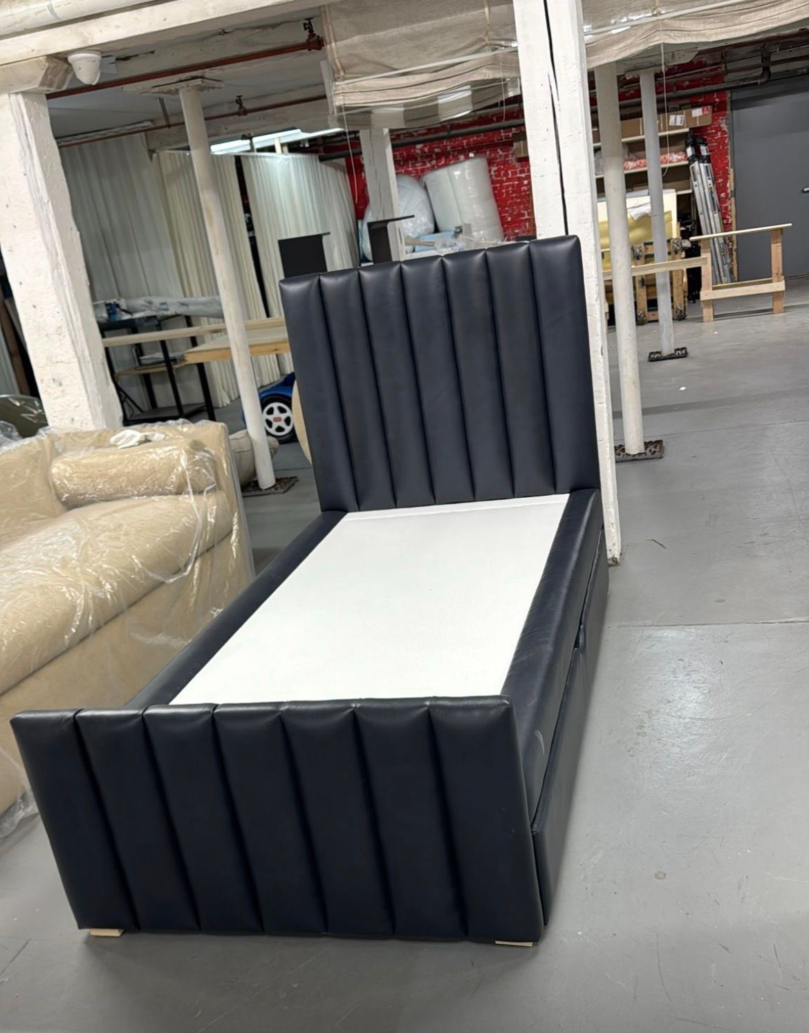 Dark blue upholstered bed frame in a warehouse setting.