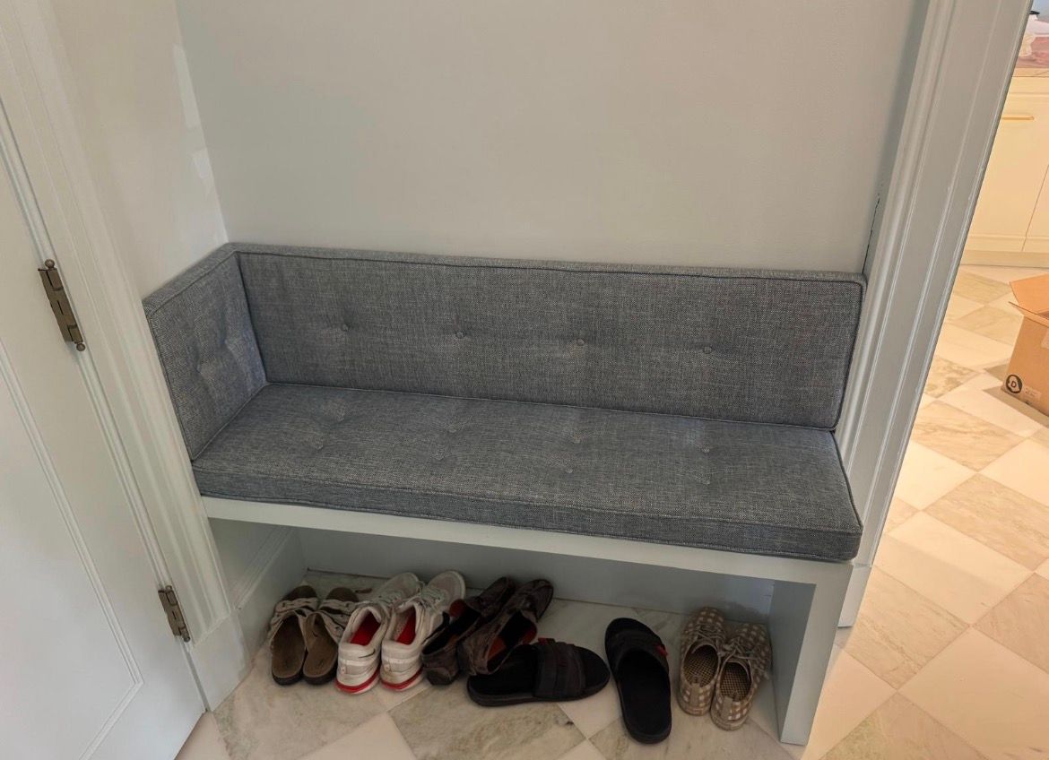 Built-in bench with gray cushion and shoe storage below in a hallway.