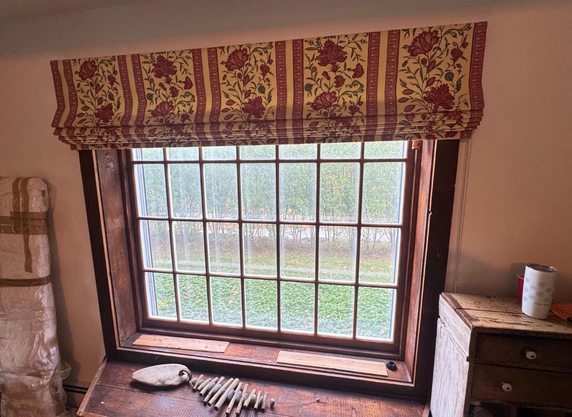 Window with a red floral valance, dark wood frame, and gridded glass. A wooden desk is below.