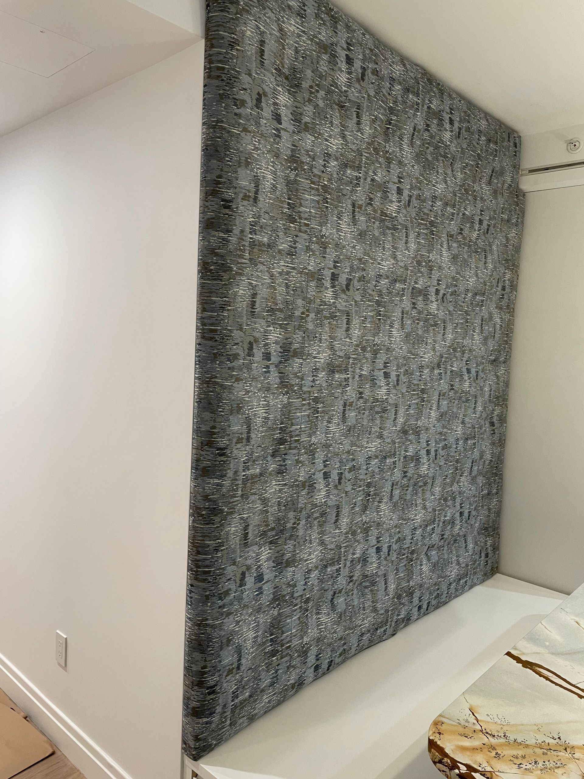 Gray soundproofing material on a wall corner, next to a white wall.