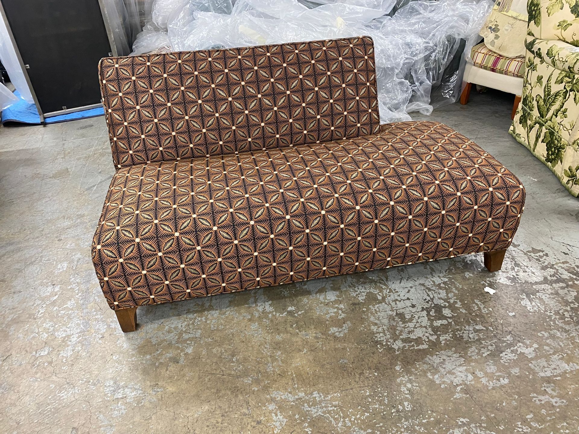Brown patterned loveseat with wooden legs, in a warehouse setting.