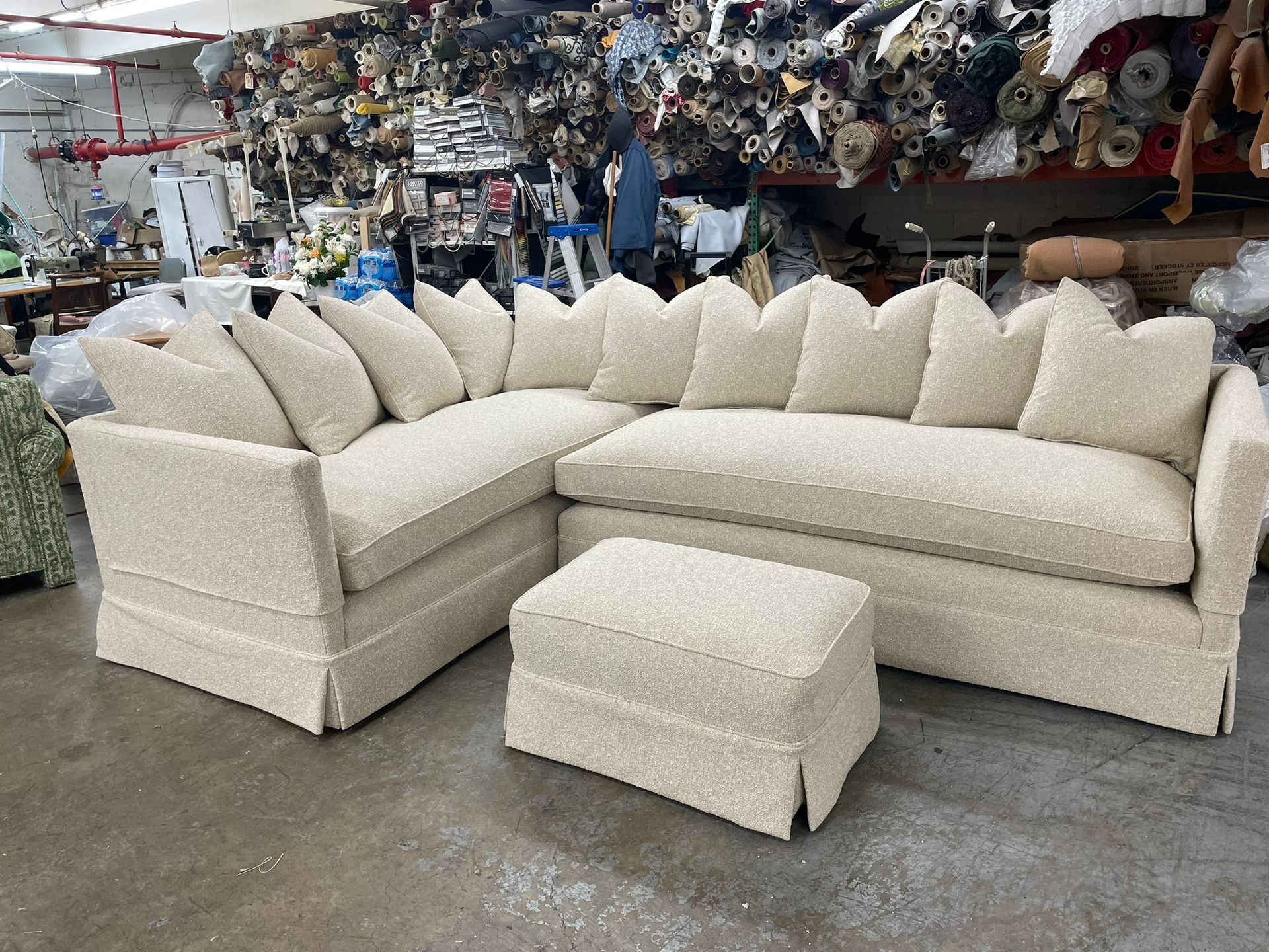 Cream-colored sectional sofa with matching ottoman in a warehouse setting.