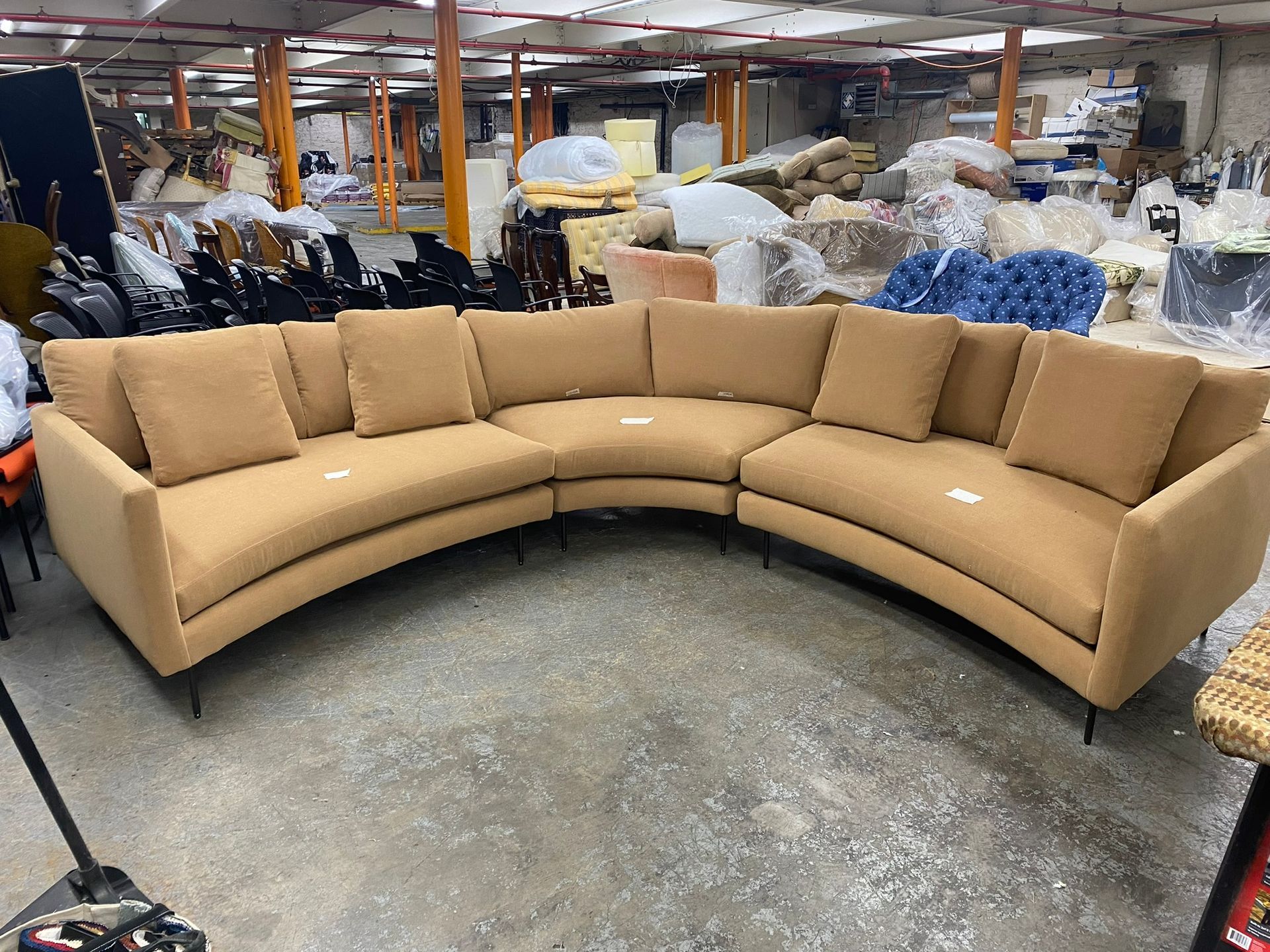 Curved tan sofa with black legs and matching pillows in an industrial setting.