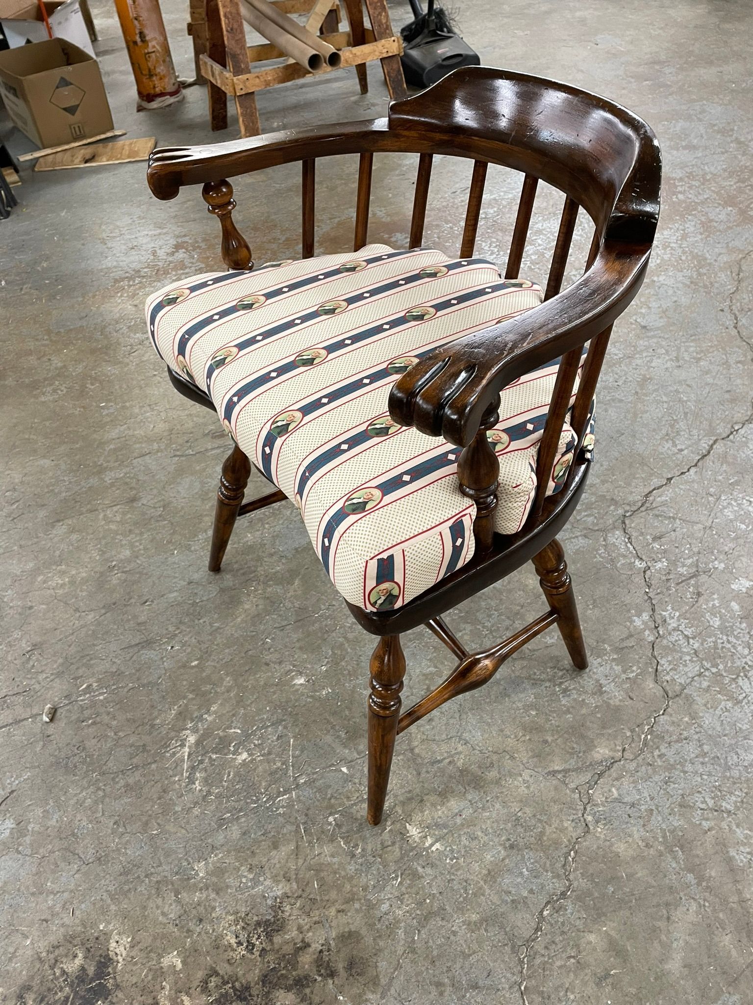 Wooden captain's chair with striped cushion in a workshop setting.