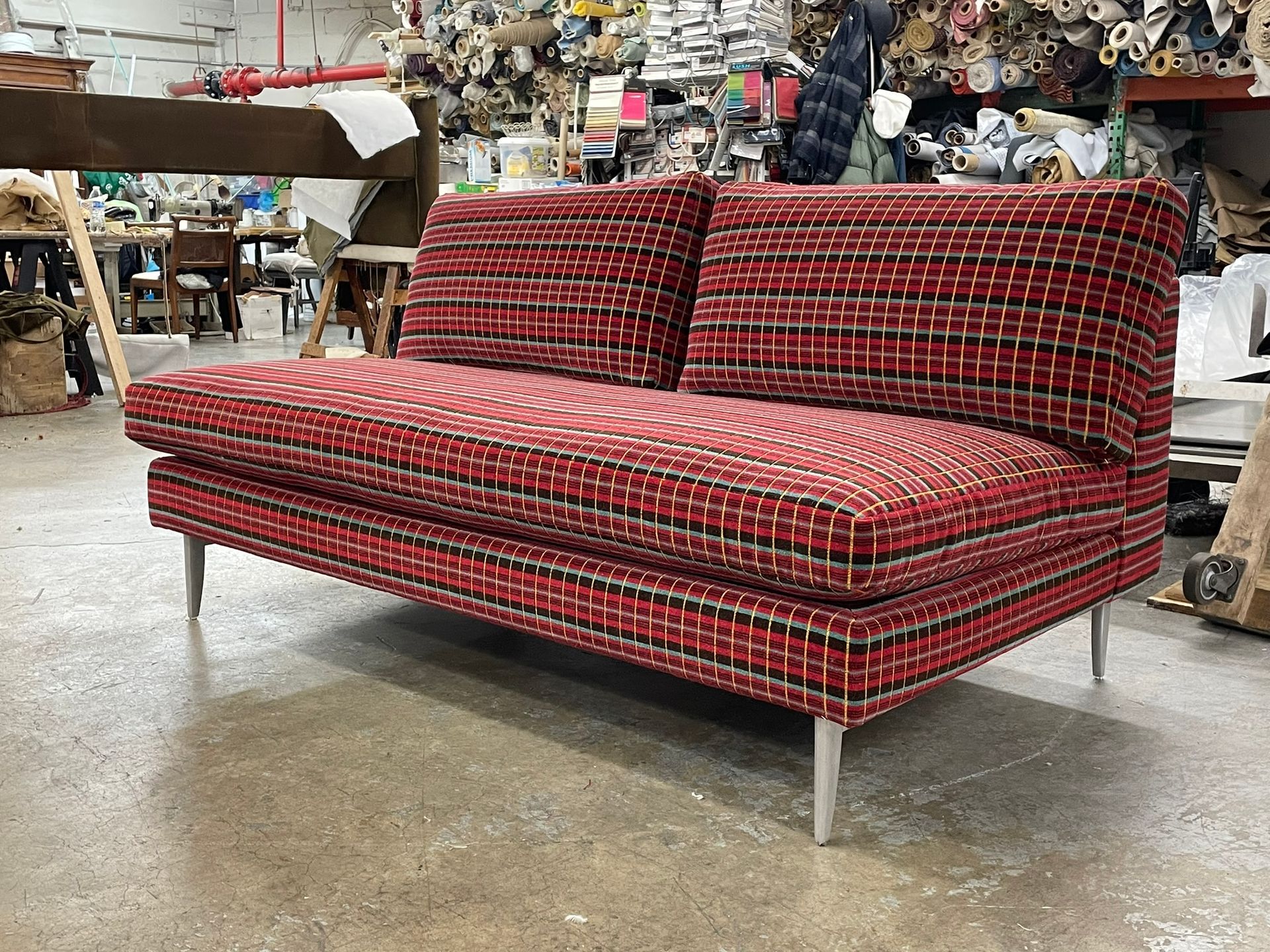 Red and black woven fabric loveseat with silver legs in an industrial workshop.