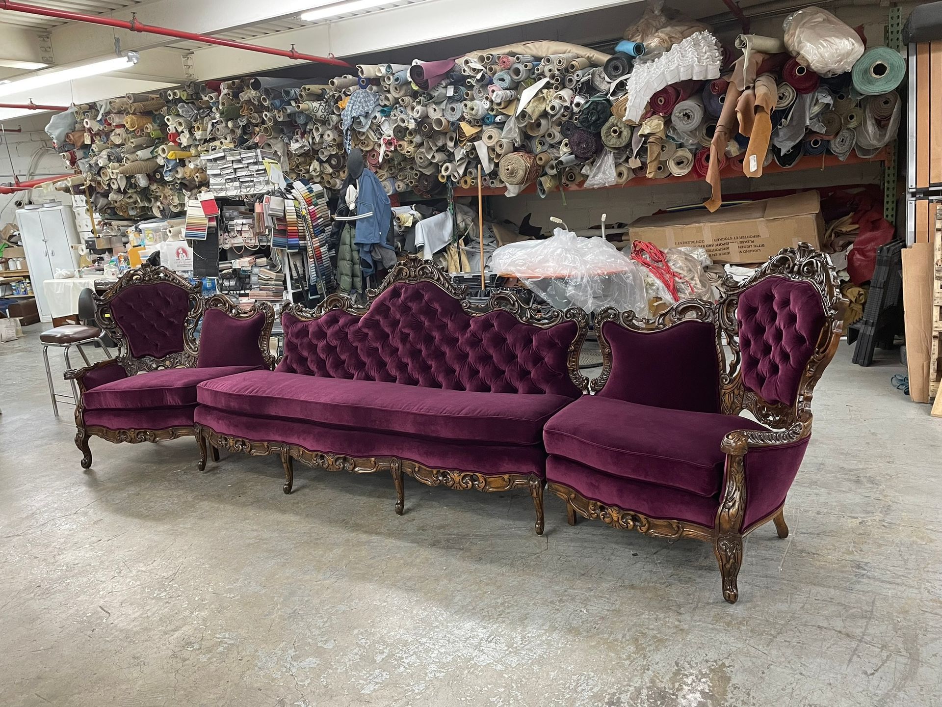 A luxurious, antique velvet sofa and chairs in a workshop, against a backdrop of fabric and materials.